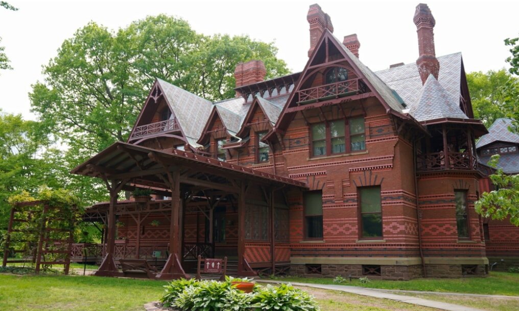 Victorian-style house with intricate brickwork and pointed roofs, surrounded by lush greenery. The scene is calm and historical in tone.