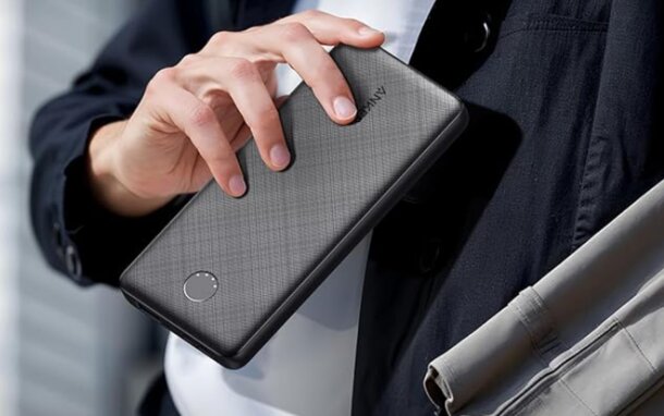 A man holding a black smartphone in his right hand, looking slightly to the side.