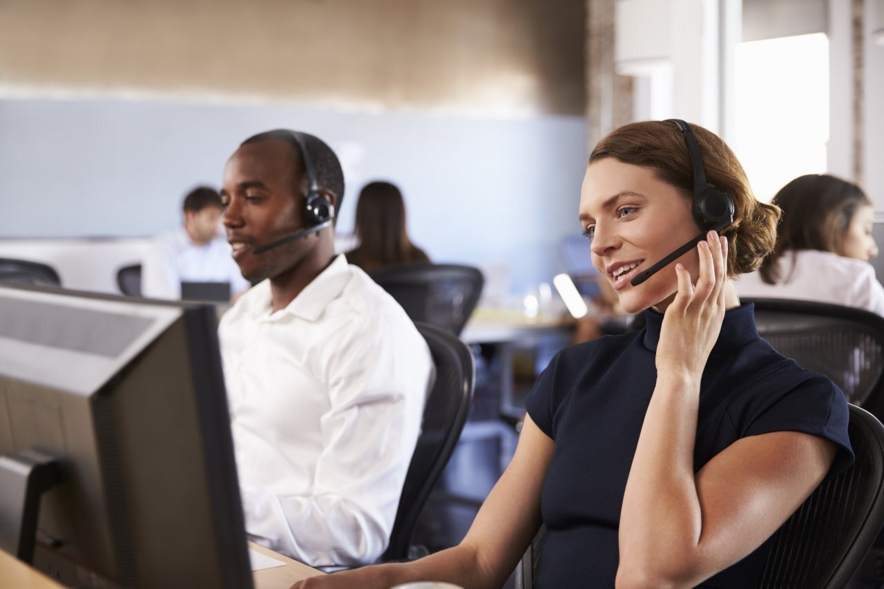 A man and woman in a call center engaged in a conversation on the phone, surrounded by office equipment and headsets.