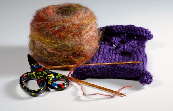 A purple bag containing a pair of scissors and a pair of knitting needles, showcasing crafting tools for creative projects.