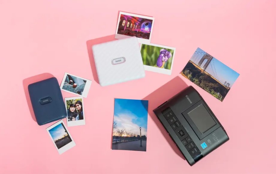 Portable photo printer, prints, and cases on a pink surface. Photos display colorful scenes, including landmarks and nature, conveying a vibrant and creative mood.