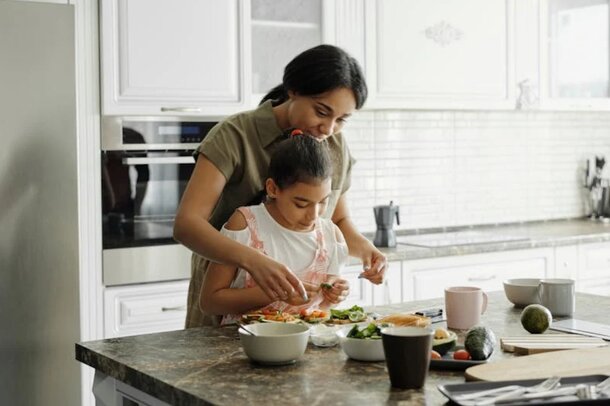  A woman and a child are cooking together in a kitchen, preparing ingredients for a meal.