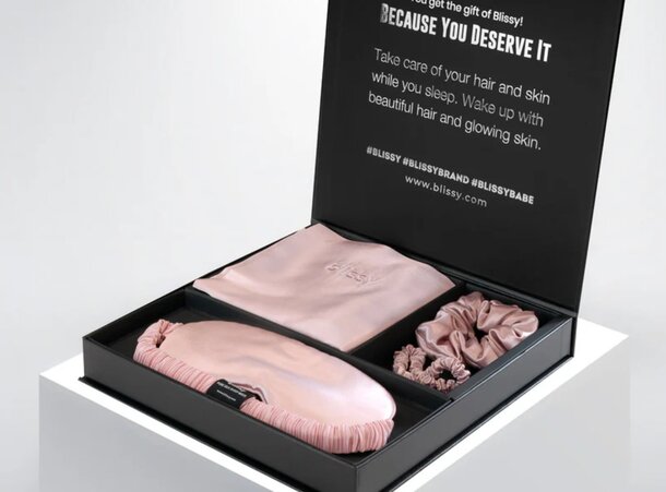 A box containing a pink silk robe, matching panties, and cozy socks arranged neatly inside.