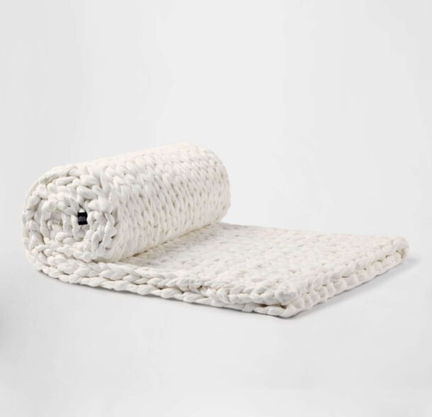 A white blanket draped with a textured white knitted cover, creating a cozy and inviting appearance.