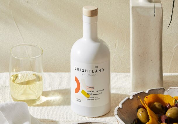 A bottle of white wine beside a bowl of green olives on a wooden table, creating a rustic dining setting.