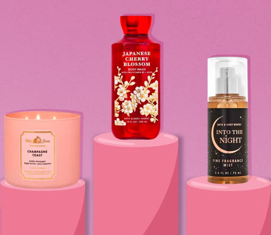 Pink background with three Bath & Body Works products on pink podiums: a Champagne Toast candle, Japanese Cherry Blossom body wash, and Into the Night fragrance mist.