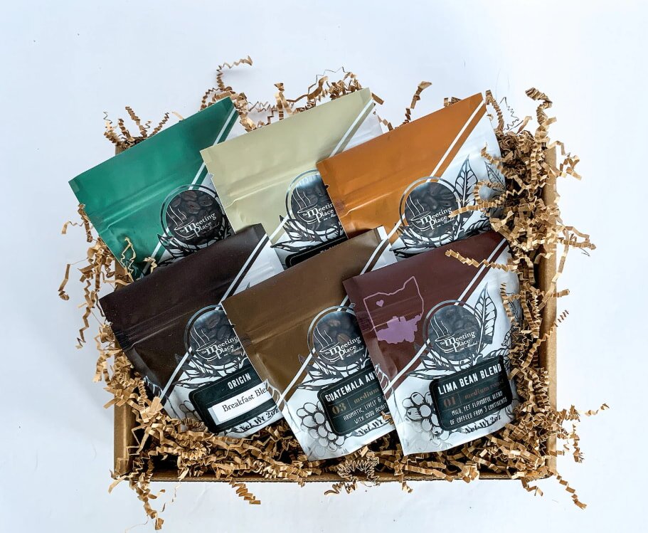 A gift box filled with six colorful bags of coffee blends, each uniquely labeled. Set against a backdrop of brown crinkle paper.