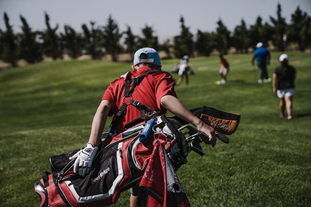 A man walking on a golf course, carrying a golf bag over his shoulder.