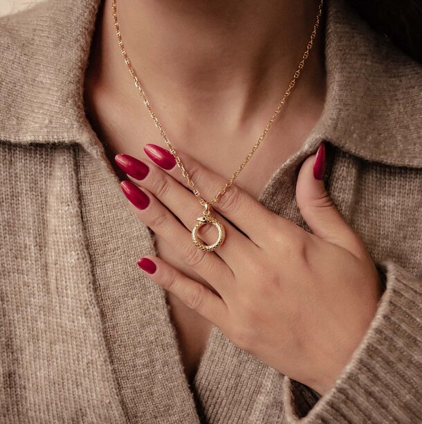 A woman displays red nails and wears a gold necklace, showcasing her elegant style and attention to detail.  