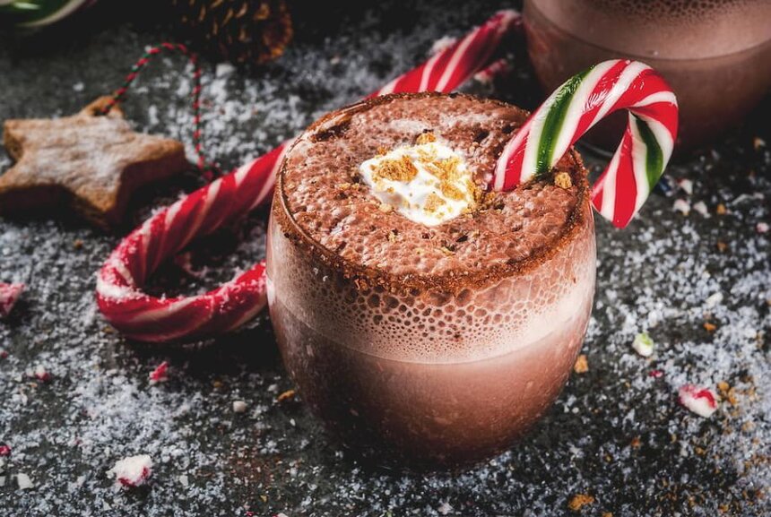 Two mugs of hot chocolate topped with whipped cream and candy canes, set against a festive background.