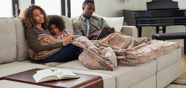 A family sits together on a couch, wrapped in a cozy blanket, enjoying each other's company.