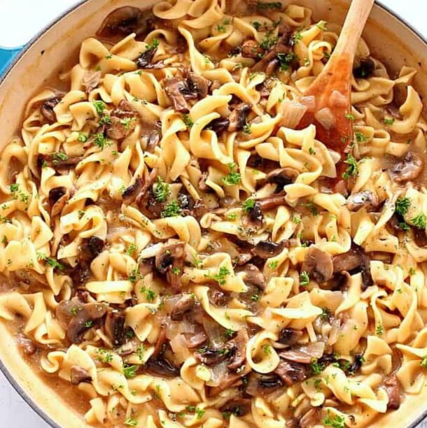 A pan of creamy mushroom pasta with a wooden spoon resting inside, ready to be served.