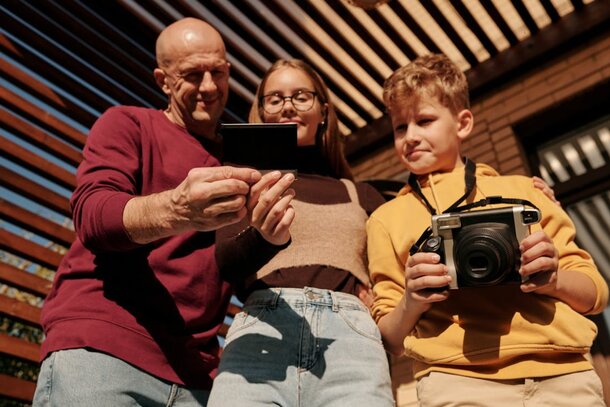 A family smiles together while taking pictures with a digital camera outdoors.