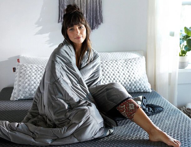 A woman sits on a bed, wrapped in a cozy blanket, creating a serene and comfortable atmosphere.