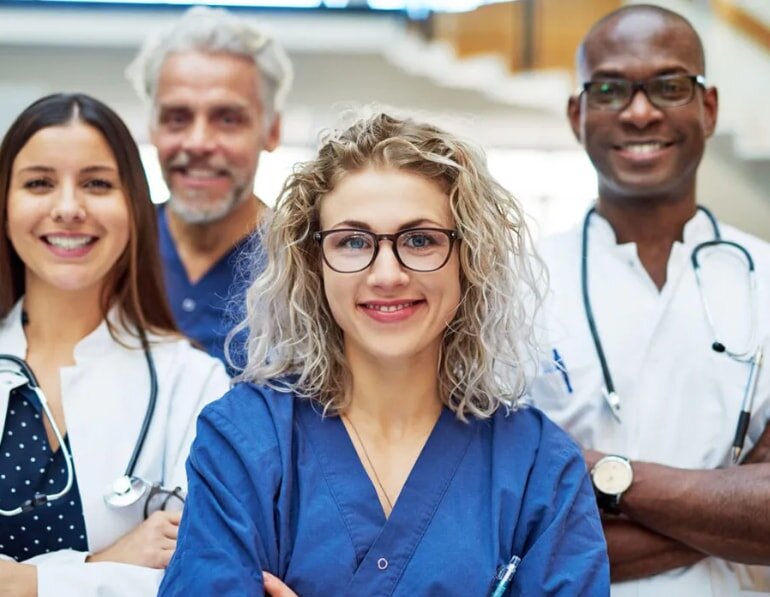 A group of doctors in white coats standing together, smiling and engaged in conversation in a hospital setting.