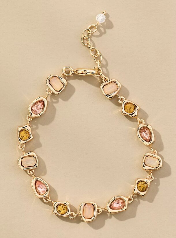A gold tone bracelet adorned with pink and yellow stones, showcasing a vibrant and elegant design.