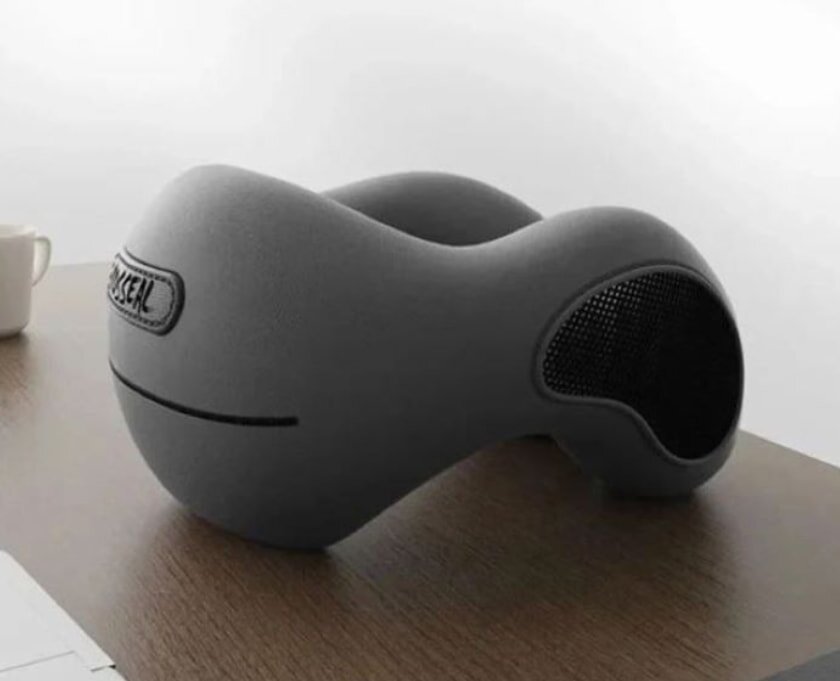 A sleek, gray memory foam pillow shaped for head support rests on a wooden desk. A white coffee cup and a minimalist background convey calm.