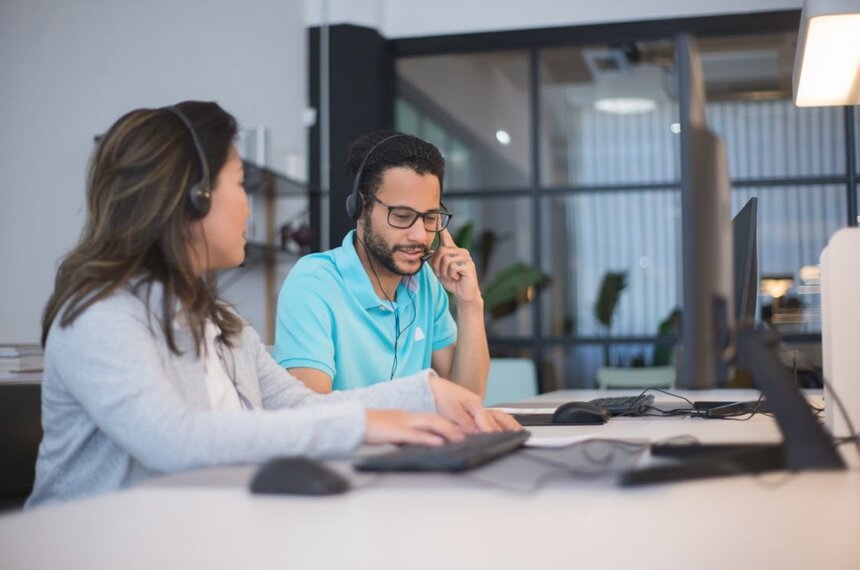 A man and woman working together in a call center, engaged in conversation while using headsets. 