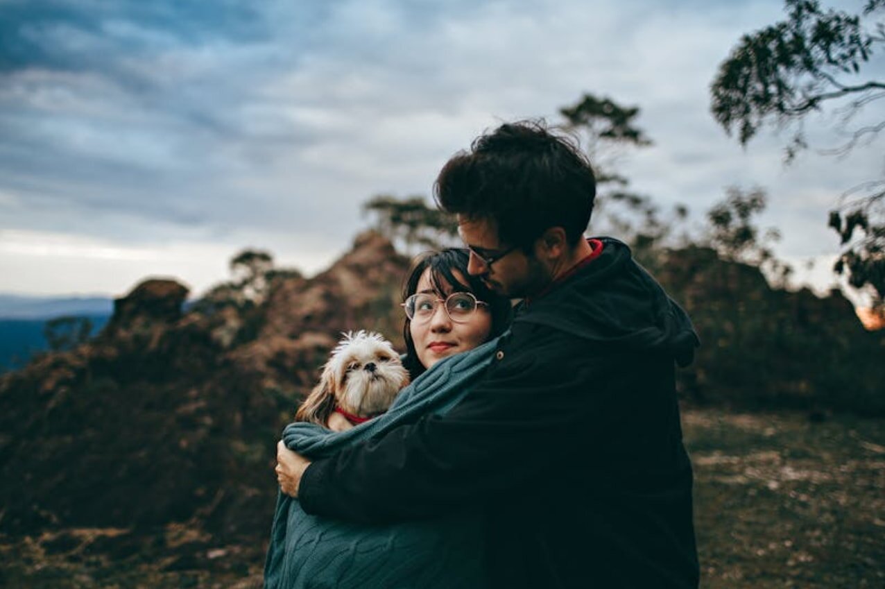 Couple embracing each other in a scenic mountain landscape, surrounded by lush greenery and distant peaks.