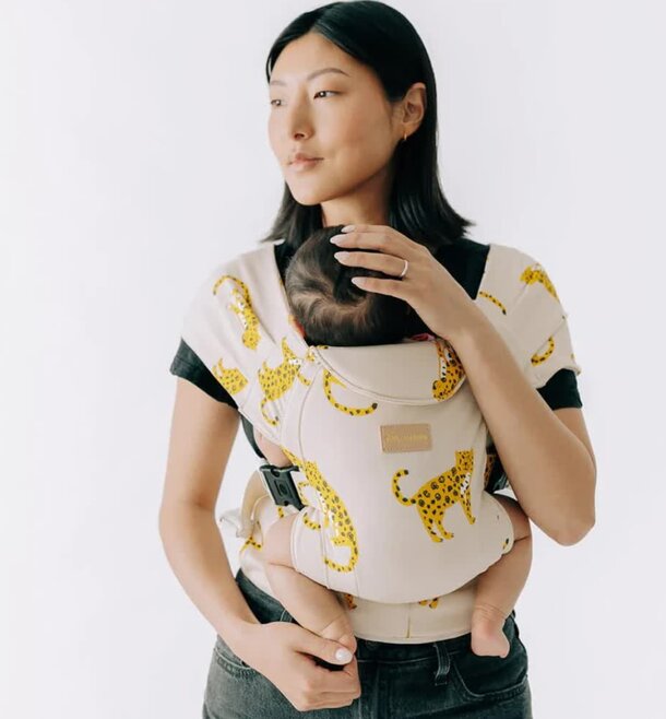 A woman wearing a yellow and black cheetah print baby carrier, showcasing a stylish and playful design.