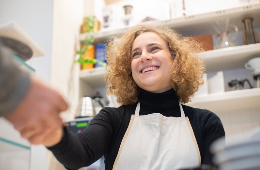 A woman shakes hands with a customer in a restaurant, showcasing a friendly and professional interaction.  