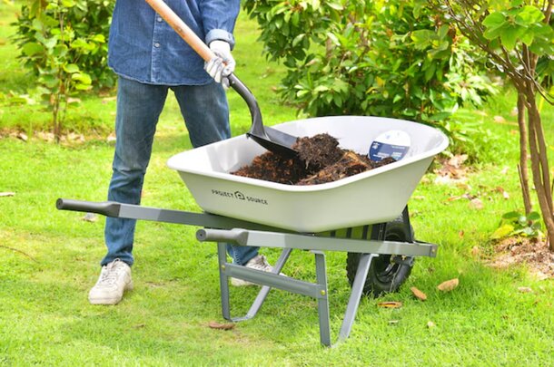A man shovels dirt into a wheelbarrow, actively engaged in landscaping or construction work outdoors.
