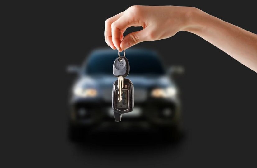 A person holds a car key against a solid black background, emphasizing the key's design and the individual's grip.