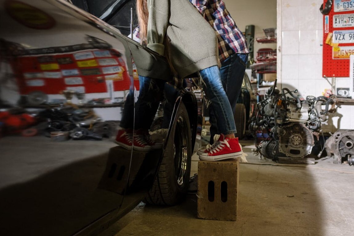 A man stands on a box in a garage, surrounded by tools and equipment, looking focused on a task.