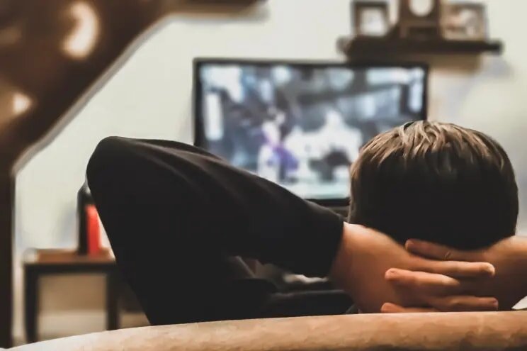 A man sits on a couch, focused on watching television in a cozy living room setting.