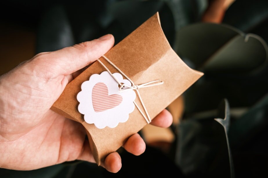 A hand holds a gift box adorned with a heart-shaped tag, symbolizing love and thoughtfulness.