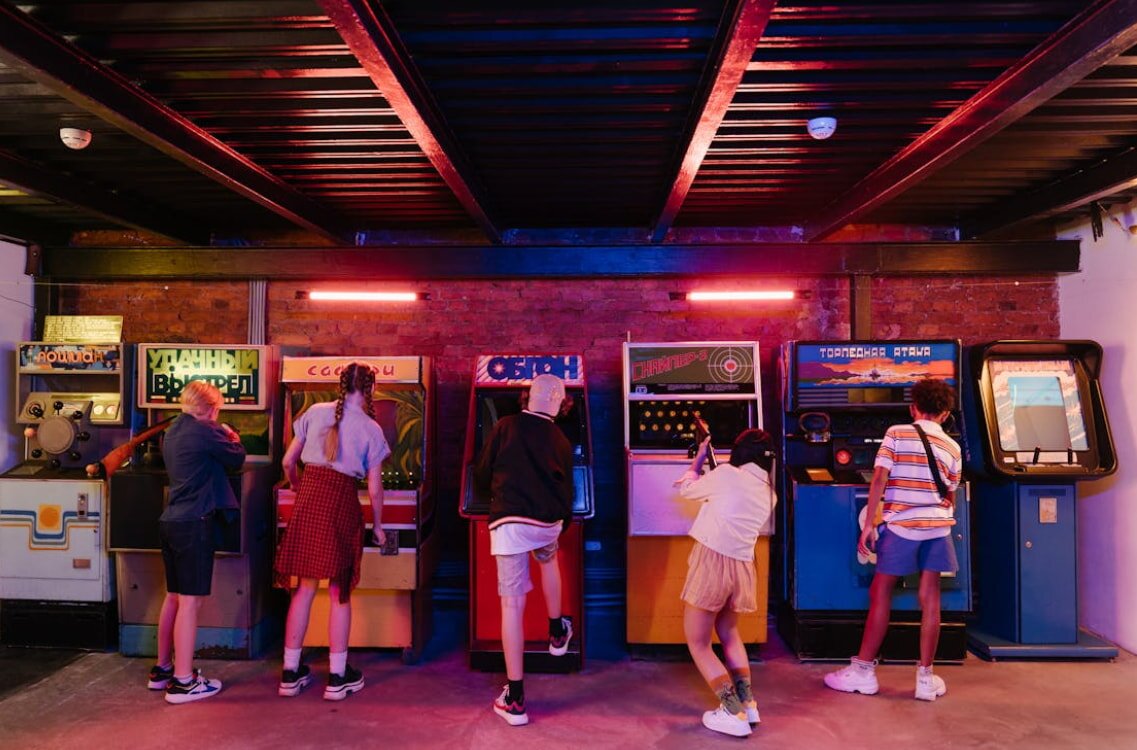 A group of people gathered around several arcade machines, engaging with the games and enjoying their time together.