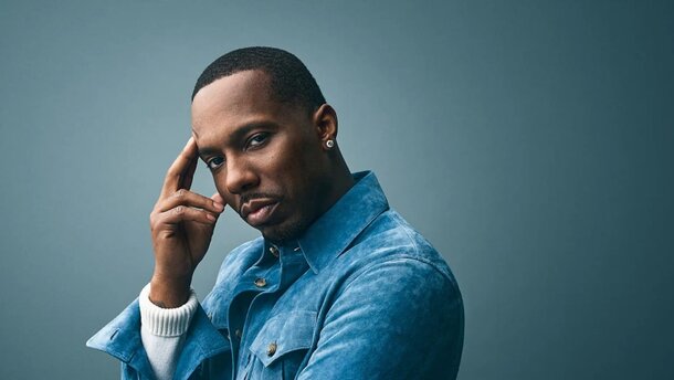 A man in a blue jacket holds his hand to his head, appearing contemplative or stressed.