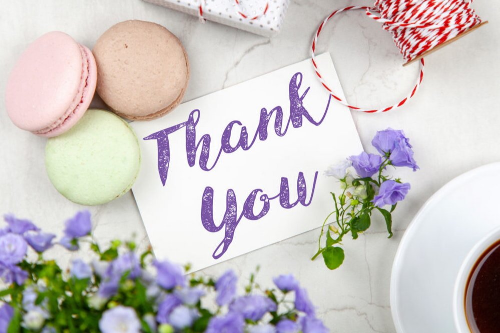 Thank you card featuring colorful flowers alongside a steaming cup of coffee on a wooden table.