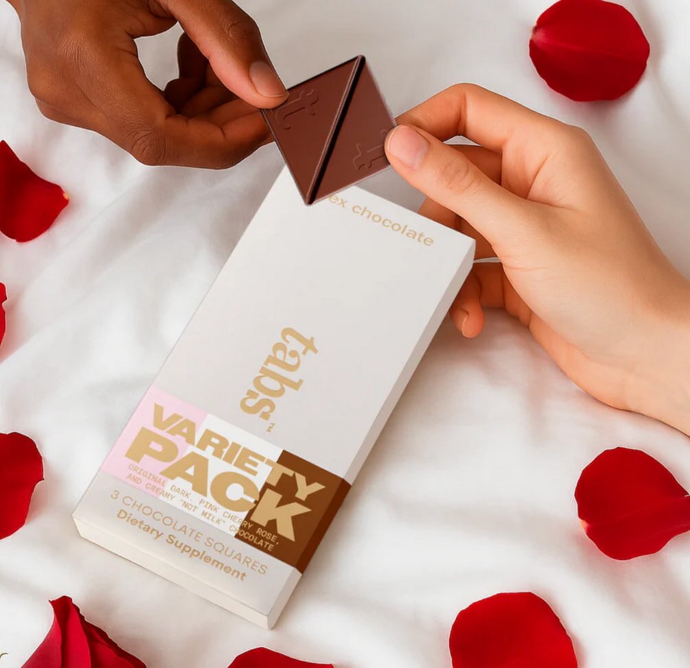 A woman holds a chocolate bar beside a delicate rose petal, creating a contrast of sweetness and beauty.