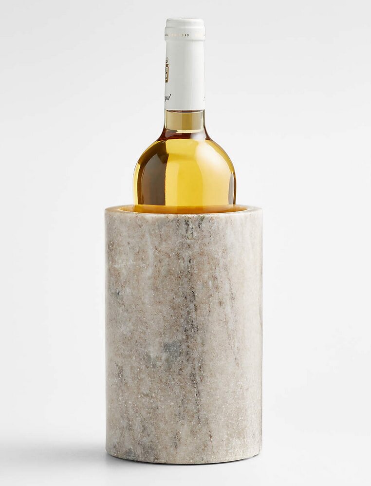 A marble wine cooler with a cylindrical design holds a bottle of white wine. The cooler's smooth, natural texture contrasts with the glossy bottle.