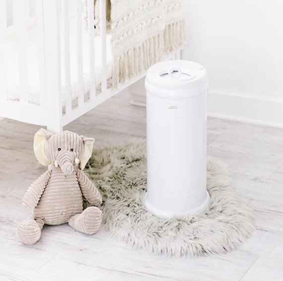 Cozy nursery scene with a tall white diaper pail on a fluffy rug beside a crib. A soft, textured elephant toy sits nearby, enhancing the serene atmosphere.