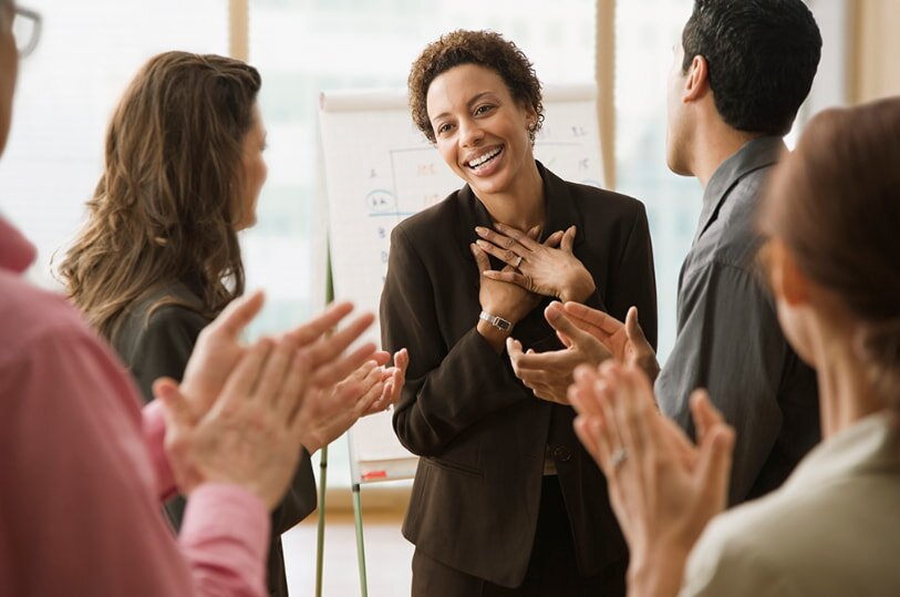 A diverse group of people clapping and smiling enthusiastically at a conference, celebrating a presentation or speaker.