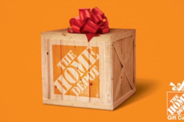 A wooden crate with The Home Depot logo, topped with a red bow, sits against an orange background, conveying a festive gift theme.