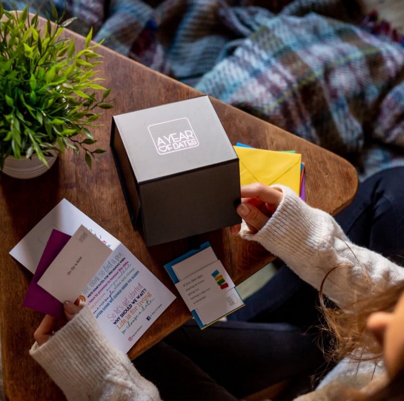 A woman sits at a wooden table, examining a box of cards placed in front of her.  