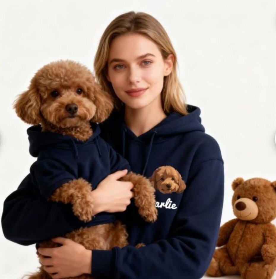 Woman smiling, holding a brown poodle, both in matching navy hoodies. A teddy bear is in the background. The scene conveys warmth and companionship.