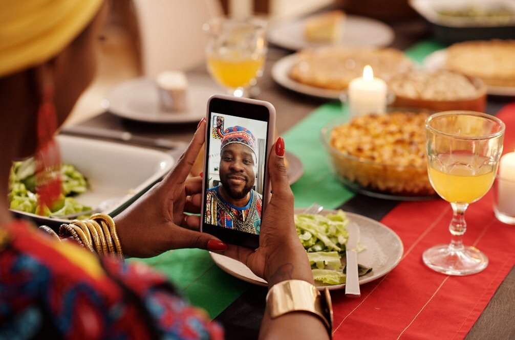 A woman sits at a table with food, video calling with a man.