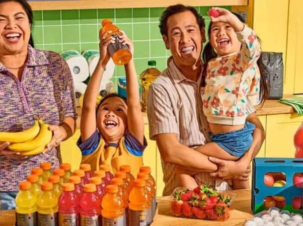 A smiling family holds various fruits and juice, showcasing their enjoyment of healthy snacks together.