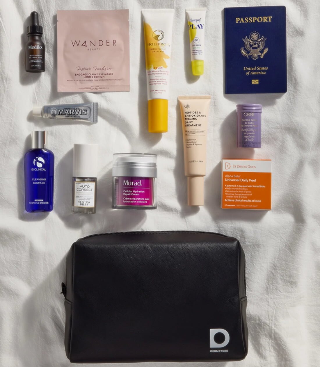 A travel bag unpacked on a bed, displaying clothes, toiletries, and travel accessories scattered around.