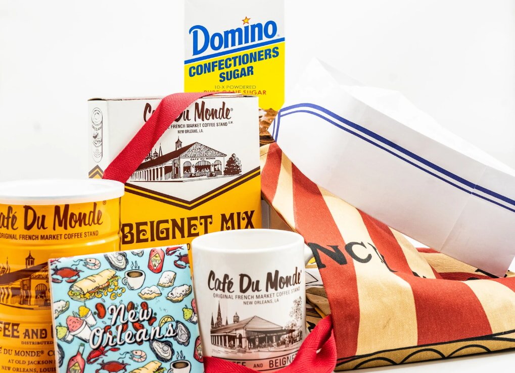 A New Orleans gift set featuring Café Du Monde items, including beignet mix, a mug, a colorful New Orleans magnet, and Domino confectioners sugar. Festive and inviting.