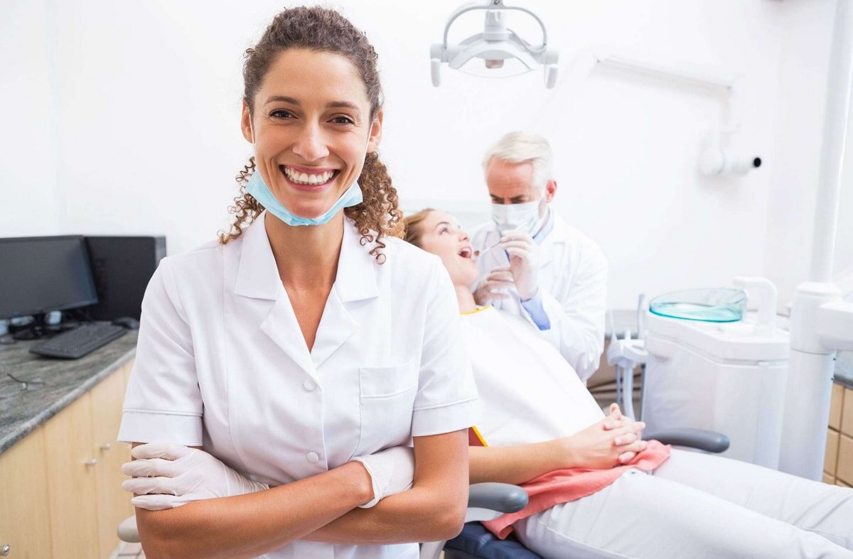 Dentist assistant smiling in dental office with patient and doctor