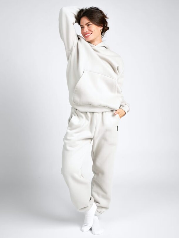 A woman wearing a grey sweatshirt and sweatpants stands casually, showcasing a relaxed and comfortable outfit.