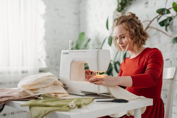 A woman focused on sewing fabric using a sewing machine in a well-lit workspace.