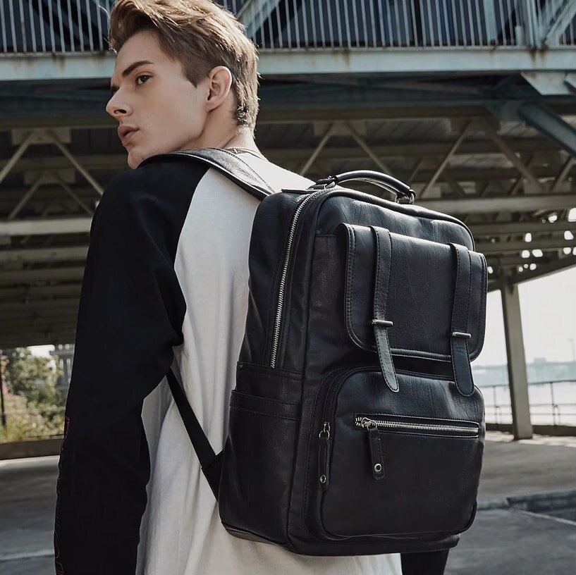 Young man with short brown hair wearing black and white shirt with large black leather backpack