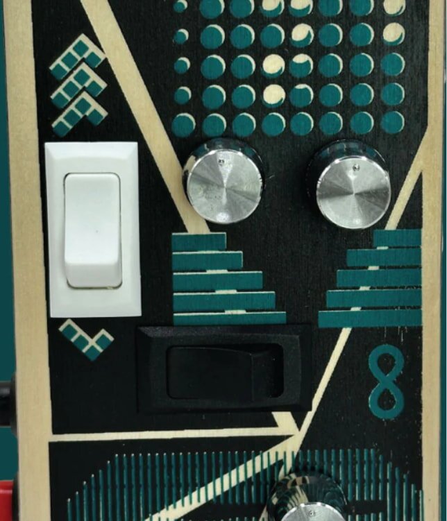 Close-up of a decorative panel with geometric patterns in teal and cream, featuring two metallic knobs, and black and white switches. Energetic and modern vibe.