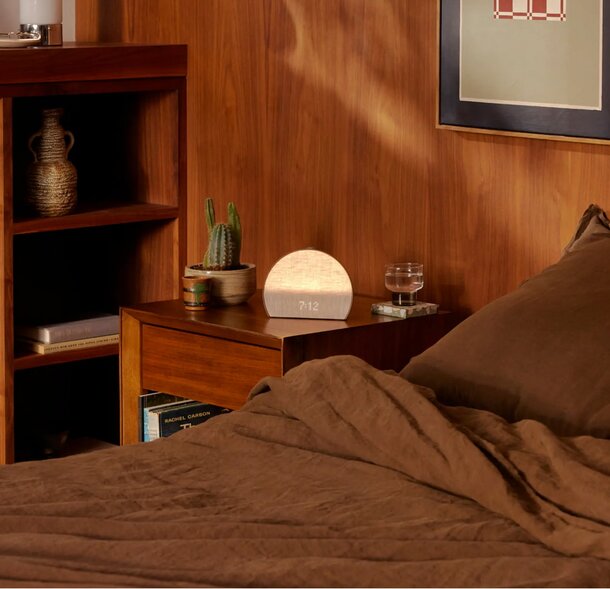 A cozy bed with a lamp on the nightstand and a book resting beside it, creating a warm, inviting atmosphere.